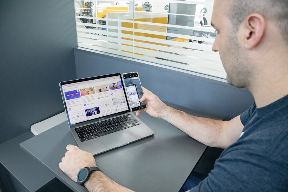 A man multitasking with a laptop and smartphone in a contemporary office space